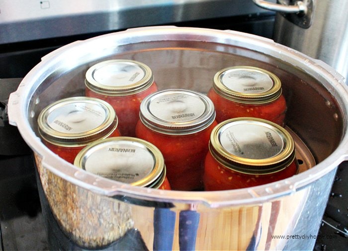 Six jars of canned tomatoes covered submerged in water for canning.