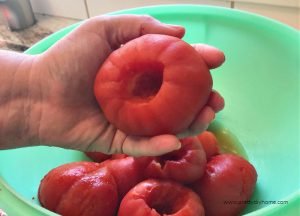 A large tomato that is having the skin and stem removed for canning tomatoes