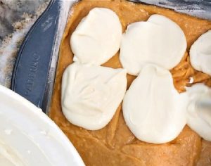 Adding dollops of cream cheese frosting to pumpkin cake batter.