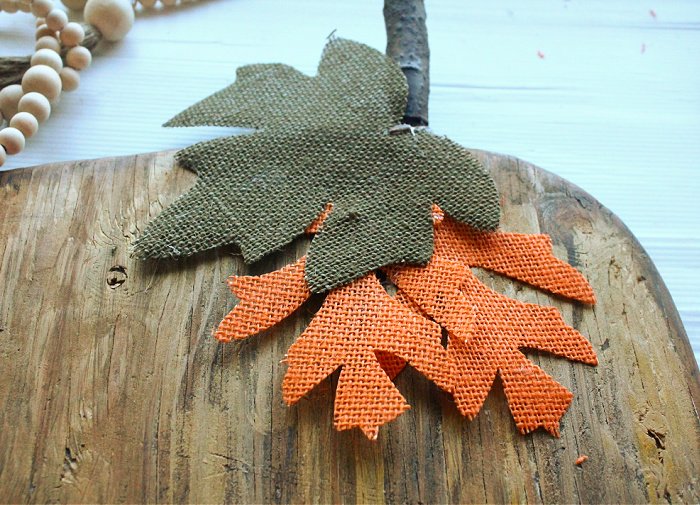 Attaching dollar store burlap leaves to a wooden pumpkin.