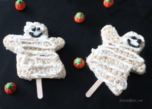 Two mummy rice krispies on sticks with black icing faces and swirls of icing wraps