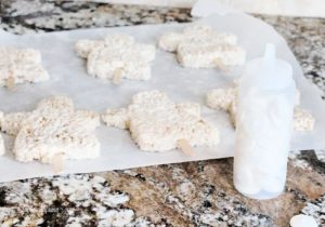 A tray of mummy rice krispie Halloween treats with popsicle sticks for easy handling.