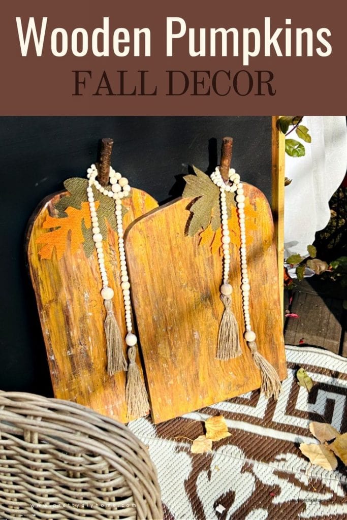 Two wood pumpkins in bright metalic colours with farmhouse beads. They are sitting on a porch with a black fall chalkboard in the background.