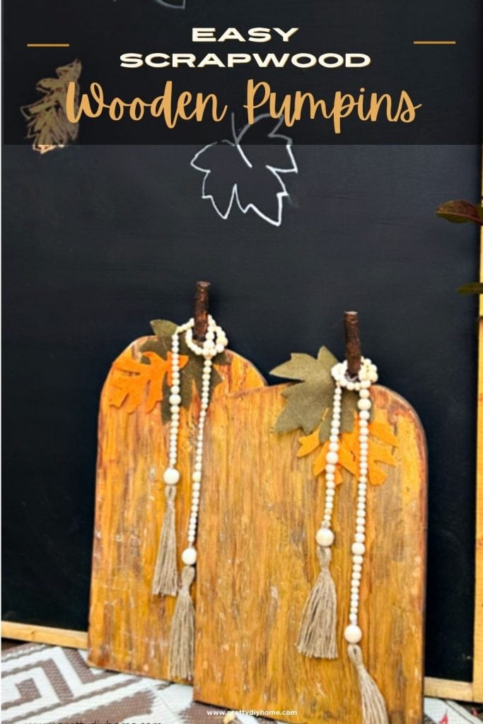 Two wooden pumpkin leaning on a black chalkboard with leaves on a outdoor porch.