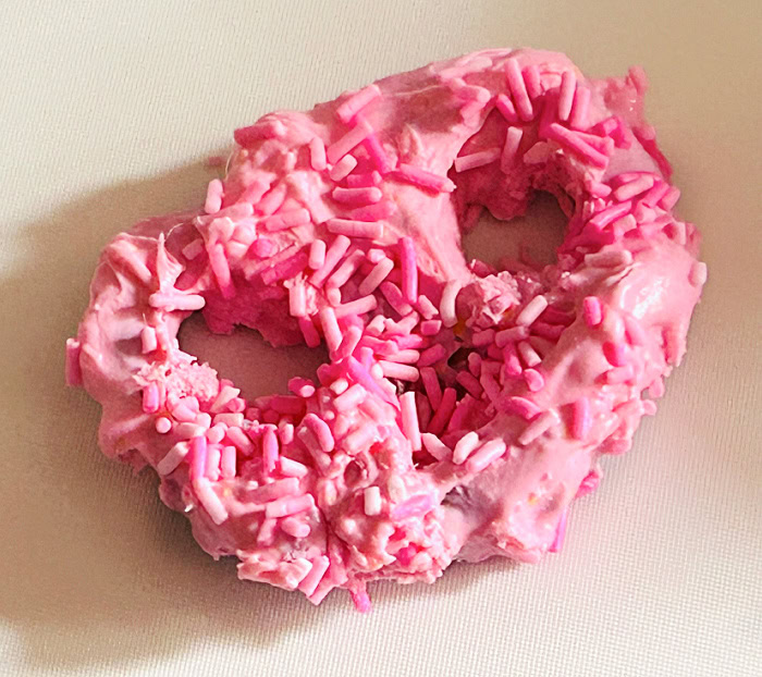 Pink Halloween monster pretzel coated in pink candy melts and matching sprinkles before adding candy eyes and licorice fangs.