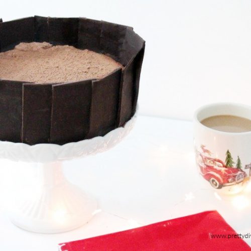 A finished no-bake chocolate cheesecake coated with cocoa. The sides of the no-bake chocolate cheesecake are decorated with a homemade chocolate collar.