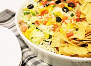 7 layer bean dip in a white bowl with a stack of tortilla chips beside.