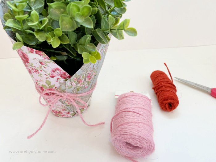 Tying a pretty twine ribbon around a Valentine's day gift idea. The Valentine's gift is a potted plant wrapped in pretty blue and pink floral cardstock.