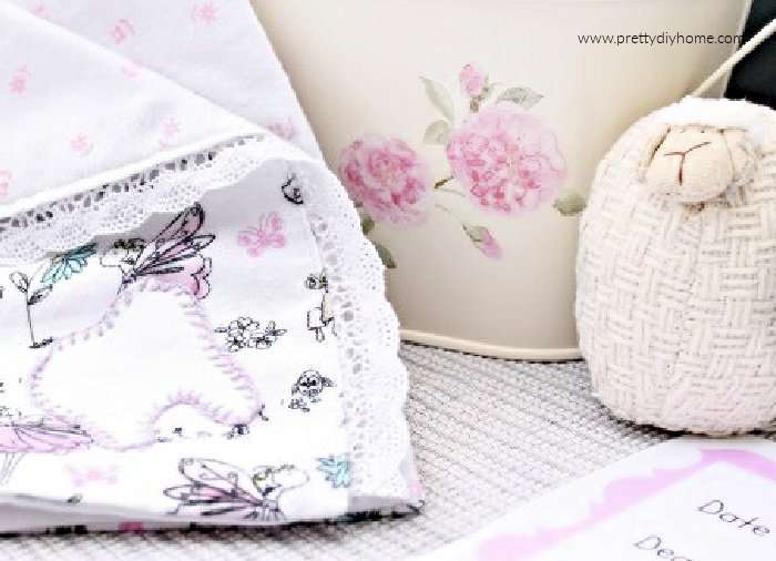 A tooth fairy tooth holder blanket with pocket, and the corner of a tooth fairy letter printable. There is a baby sheep ornament in soft cotton and a floral background vase.