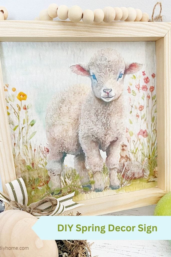 A spring diy decor sin in natural coloured wood. The sign has a pretty watercolour lamb printable standing among flowers.