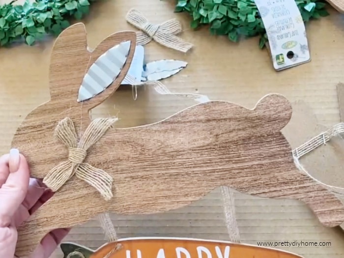 A DIY wood Easter bunny from the dollar store before painting, The bunny is part of a plaque and has wood grain finish, metal ears and a burlap ribbon.