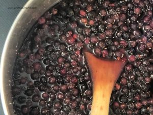 Pressing blueberries with a wooden spoon while making a simple syrup for blueberry mint lemonade mocktail.