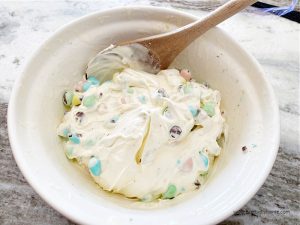 Mixing softened vanilla ice cream with chocolate mini eggs in a large bowl.