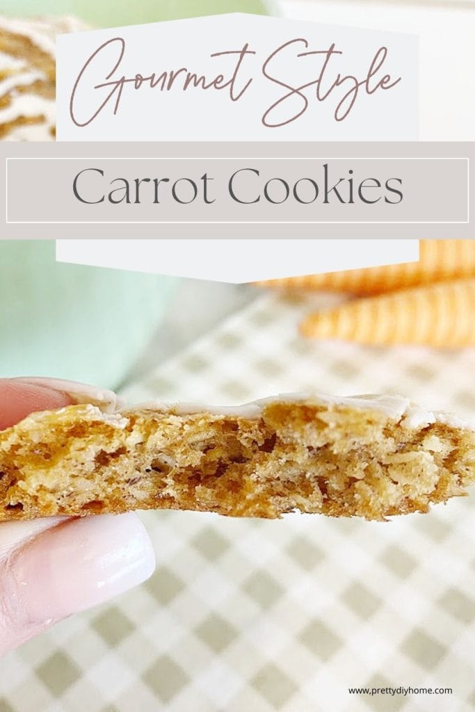 A close up of an amazing carrot cookie is broken in half and held by hand so you can see the soft chewy center. There is a soft green bowl of carrot cookies in the background and a green checkers tea towel.