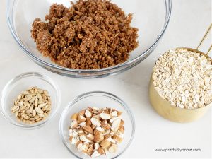 Four bowls with ingredients for homemade granola that will be part of a yogurt parfait. A bowl with prunes and spices, a bowl of oats, a bowl of coarsely chopped almonds and a bowl of sunflower seeds.