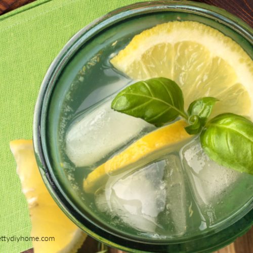 A chilled glass filled with lemon spritzer garnished with lemon slices and mint and served on a dark cuttingboard with green napkin.