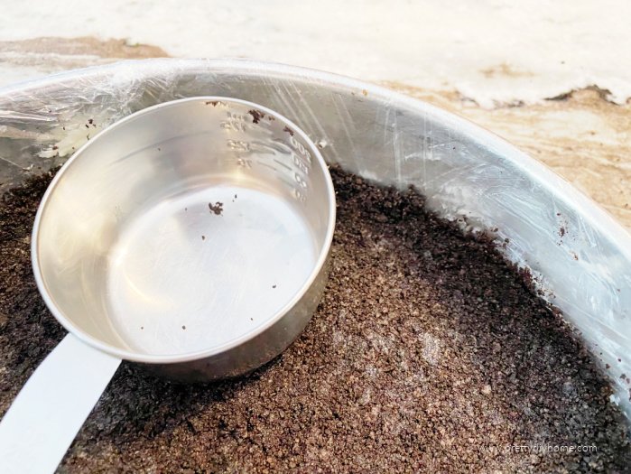 Pressing an oreo cookie crust into the bottom of a springform pan using a measuring cup.