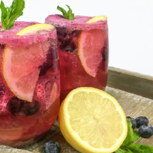 Two glasses filled with ice, lemon slice, crushed mint and blueberry lemonade.