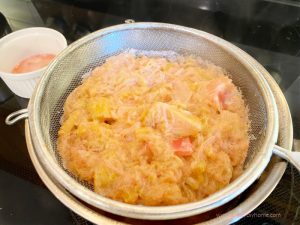 A saucepan with a sieve full of cooked rhubarb over it.