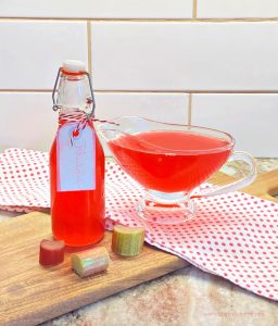 A bottle filled with homemade rhubarb syrup recipe and a bowl of rhubarb syrup beside it.