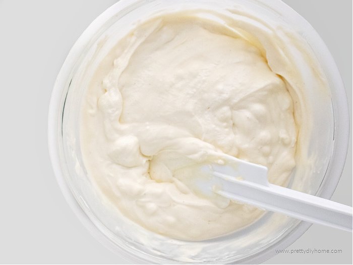 Whipped whipping cream in a clear glass bowl. The bowl has a white spatula inside