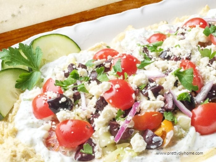Greek dip with hummus and tzatziki topped with cucumber, tomatoes, feta, olives, and red onion.