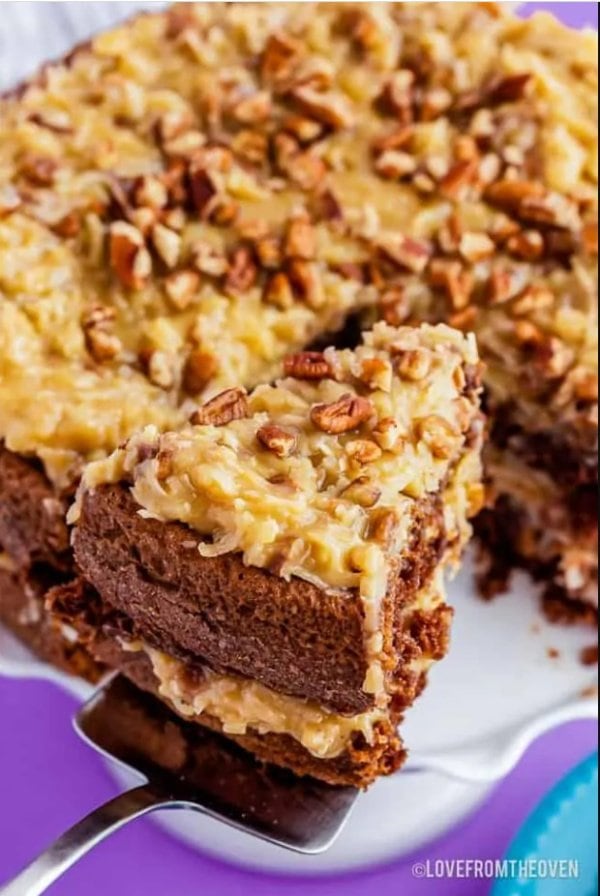 A German chocolate cake covered with coconut pecan frosting. There is a slice of cake being served so you can see the layers of cake and icing.