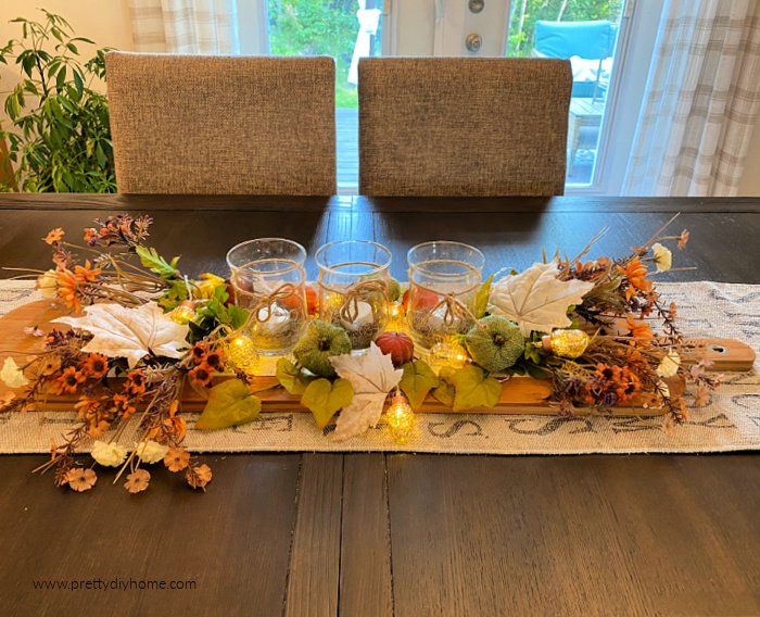 A fall centerpiece diy craft with a charcuterie board, candles, pumpkins, fall leaves and florals in soft peaches, greens and whites.