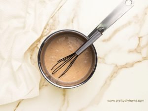 A pot of warmed pumpkin coffee creamer being set aside to cool. The pumpkin creamer is frothy and there is a whisk still in it.