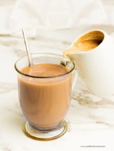 Serving pumpkin spice coffee creamer by pouring it into a clear mug of hot coffee.