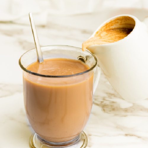 Serving pumpkin spice coffee creamer by pouring it into a clear mug of hot coffee.