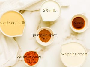 Six ingredients for pumpkin spice creamer recipe, condensed milk, milk, pumpkin spice, pumpkin puree, whipping cream and vanilla each in a small bowl. The backdrop is a cream coloured granite countertop with a white tea towel.