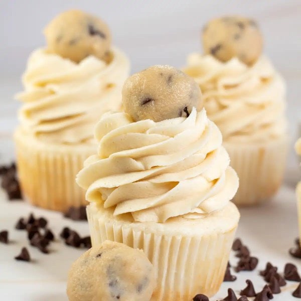 Three cupcakes covered with large swirls of chocolate chip cookie dough frosting on top.