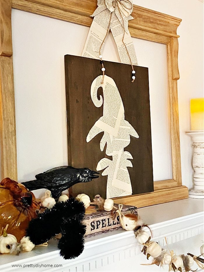 Halloween witches decor on a mantel made with a wood backdrop and a witch silhouette made with book pages. A DIY witch halloween decor idea.