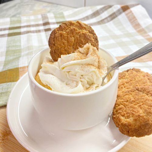 A single serving of pumpkin mousse with a swirl of whipped cream and a sprinkle of cinnamon sugar. The pumpkin dessert is served with a gingersnap stuffed into the whipped cream and another gingersnap cookie placed on the side of the serving plate.