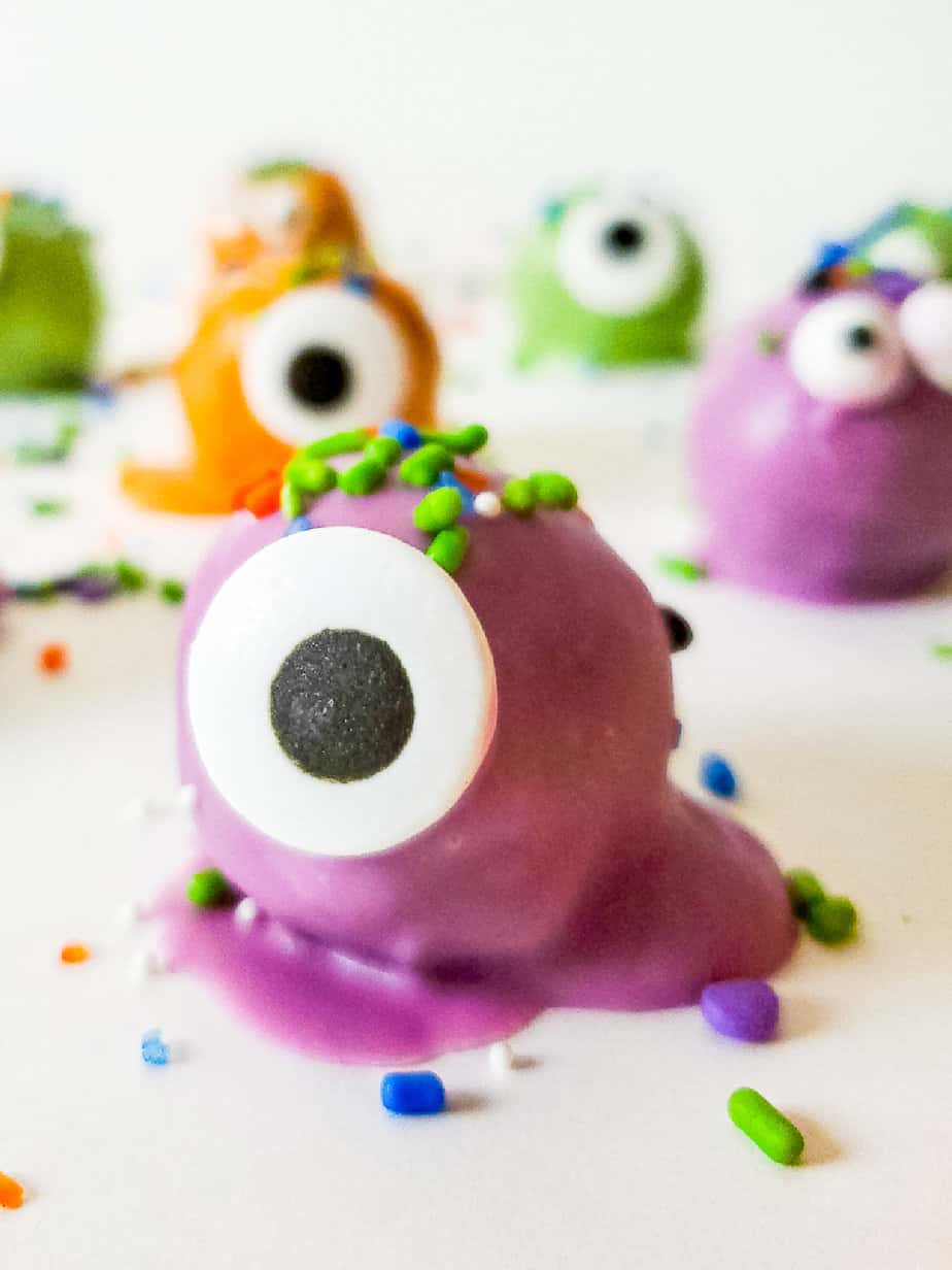 Several cute Halloween themed truffle Oreo candies, in different colors with single eyes and Halloween sprinkles hair.