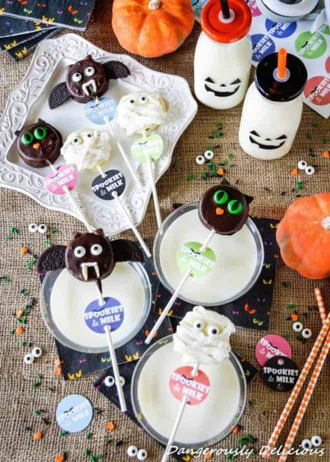 Halloween treats on a stick that look like bats, black cats, and Halloween mummies.  Each stick has a label that says spookies & Milk and they are being served across the top of a glass of milk.