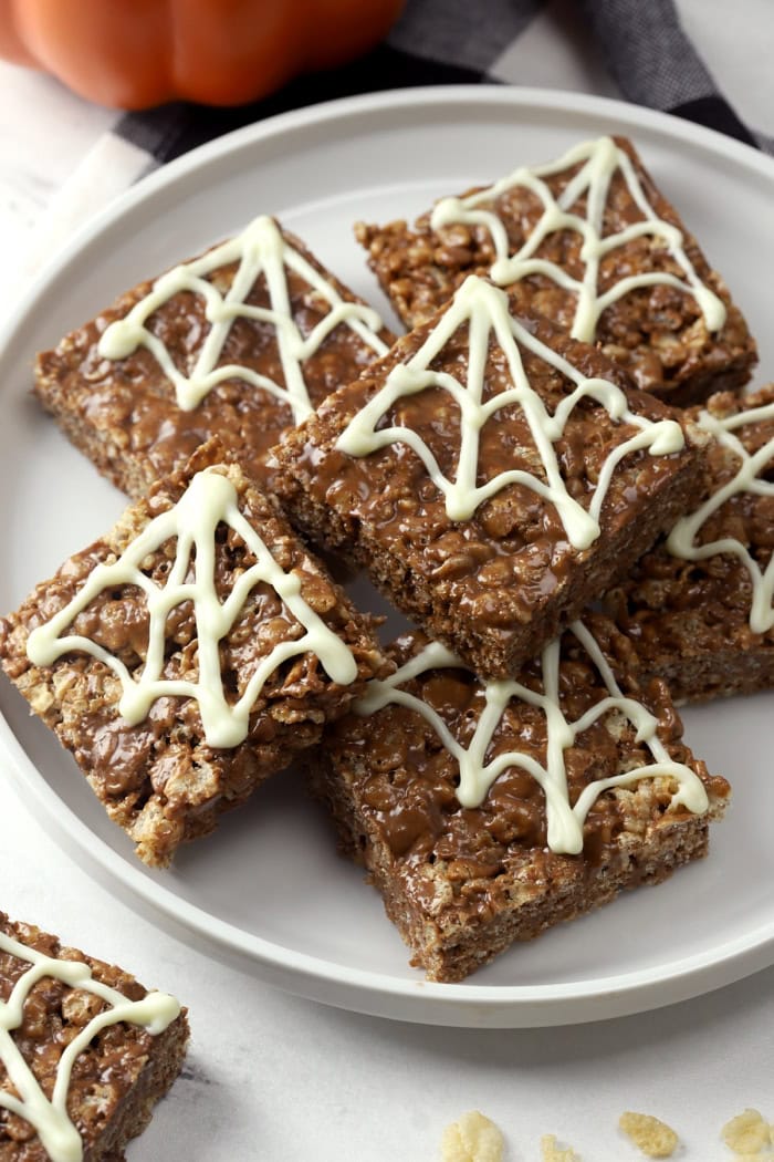 A round grey tray covered with chocolate rice krispie squares.  Each chocolate square has a white chocolate spiderweb in the corner.