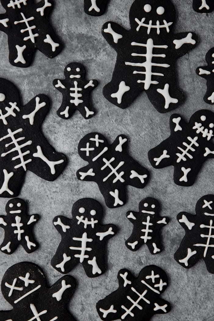 A grey slate tray covered with black cocoa skeleton cookies. The little cookies look like black gingerbread men but have very cute white skeletons on top made with icing.