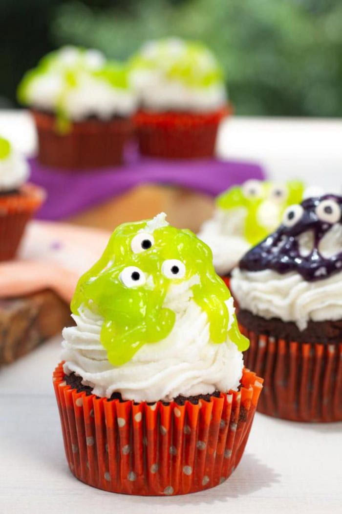 Halloween brownies served in orange cupcake wrappers.  The brownies are covered with large swirls of icing, and then either green or purple jelly on top to resemble slime.  The decorated with mini candy eyeballs.