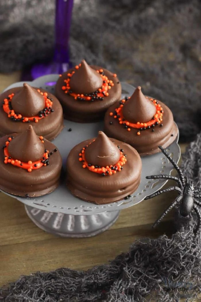 Chocolate witch hat cookies covered in milk chocolate with Hershey Kiss Tops, orange icing and Halloween sprinkles.  The Halloween cookies look like minature witch hats,