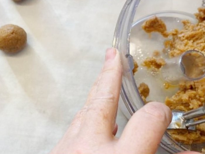 Scooping nutter butter filling with a cookie scoop before rolling and placing on cookie sheet.