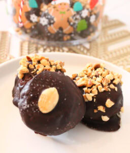 Three chocolate coated Nutter Butter peanut butter balls on a white plate, topped with peanuts.