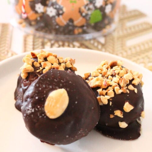 Three chocolate coated Nutter Butter peanut butter balls on a white plate, topped with peanuts.
