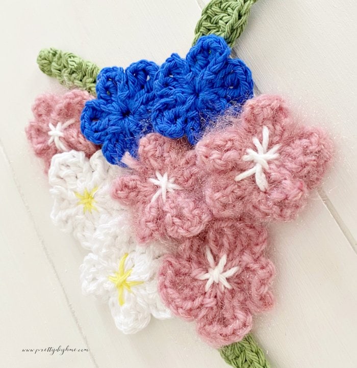 Several crocheted flowers for beginners in different colorsincluding pink dark blue yellow and white and styles all using the same easy crochet flower pattern.