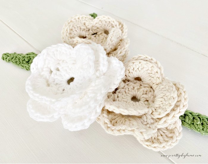 Three large crocheted roses with free patterns.  There are two cream colored rosess and one white rose.  The roses all have soft green crocheted leaves.  