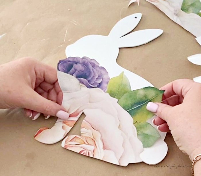 Applying a large flower sticker to the bottom half of a wooden wreath for a DIY Spring wreath idea.