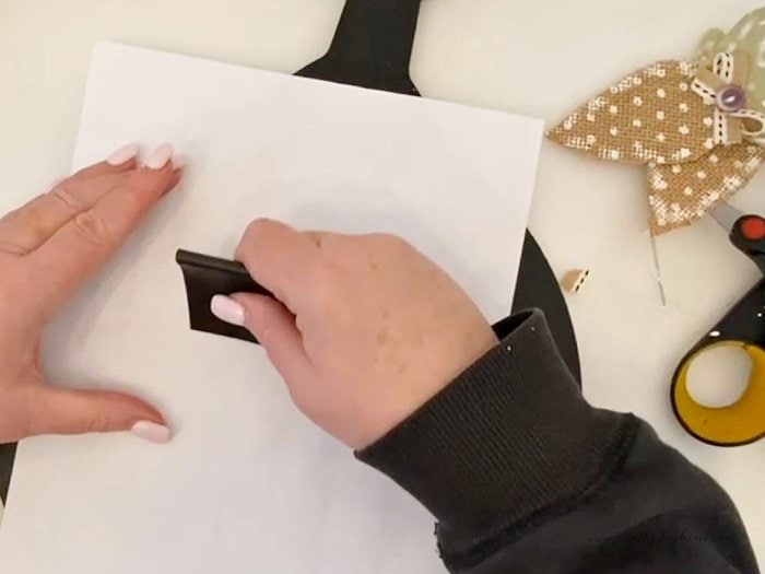 Using the corner of a scraper to transfer chalk lettering to a chalkboard.