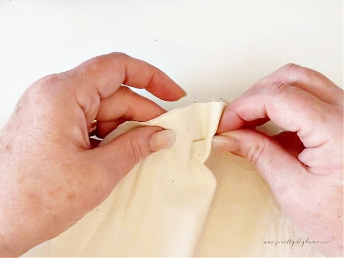 Hand stitching the raw edges of a pin cushion using a length of strong thread that will be pulled to close it.