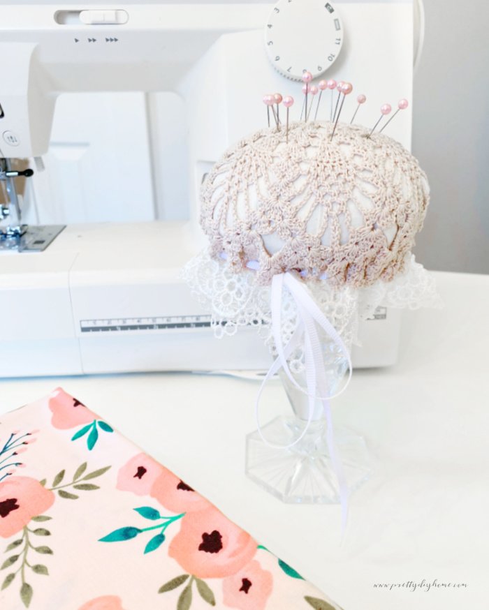 A DIY pincushion made using a vintage doily, lace and a crystal candlestick.